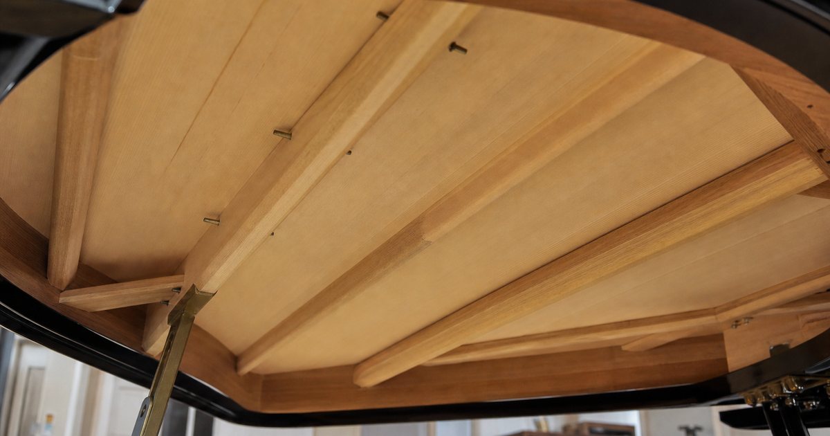 Why does soundboard material shape the tonal character of a luxury grand piano?